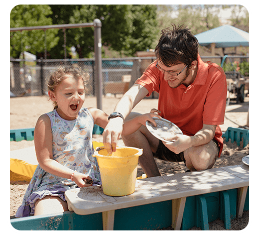 Decorative photo of Alex playing with a young girl in a sand box