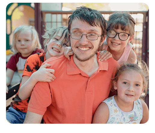 Decorative photo of Alex smiling with four children on a playground