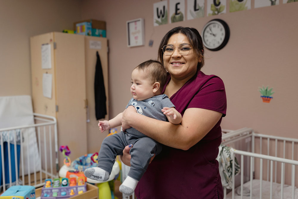 Rebecca Reyes, educadora de la primera infancia, sostiene a un bebé en un centro de cuidado infantil.